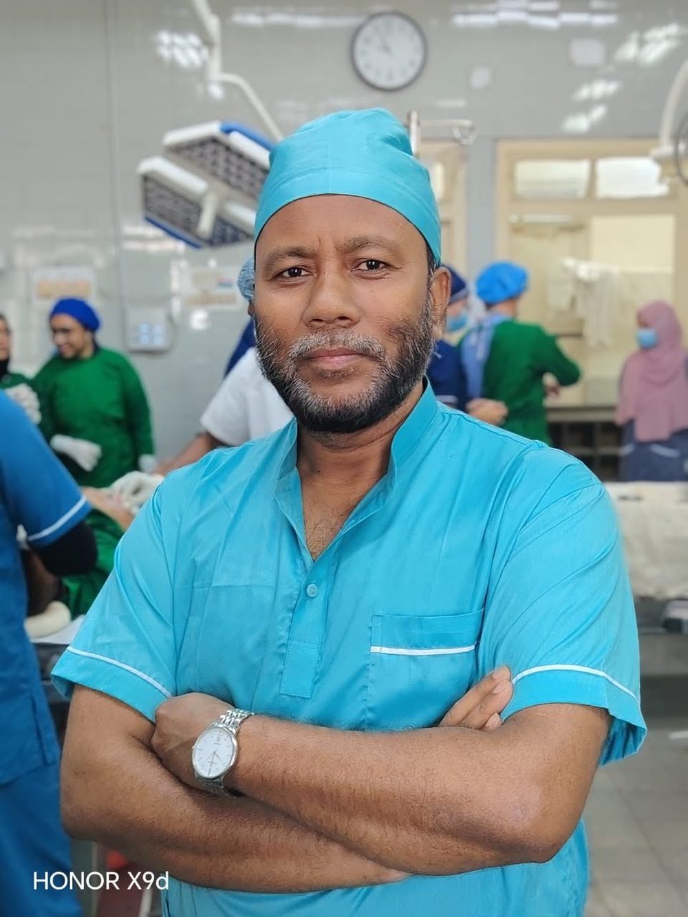Dr. Sultan Mahmud, consultant surgeon, standing in an operating theatre in surgical scrubs